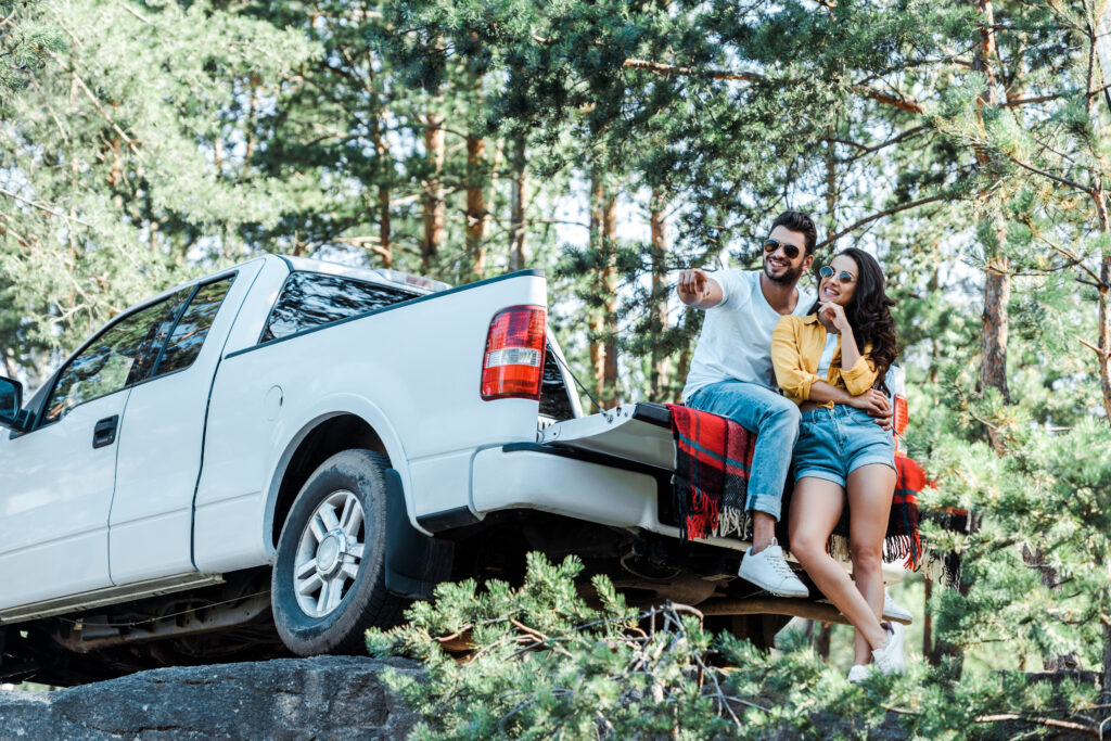 happy bearded man pointing with finger near woman in sunglasses in a truck detailing
