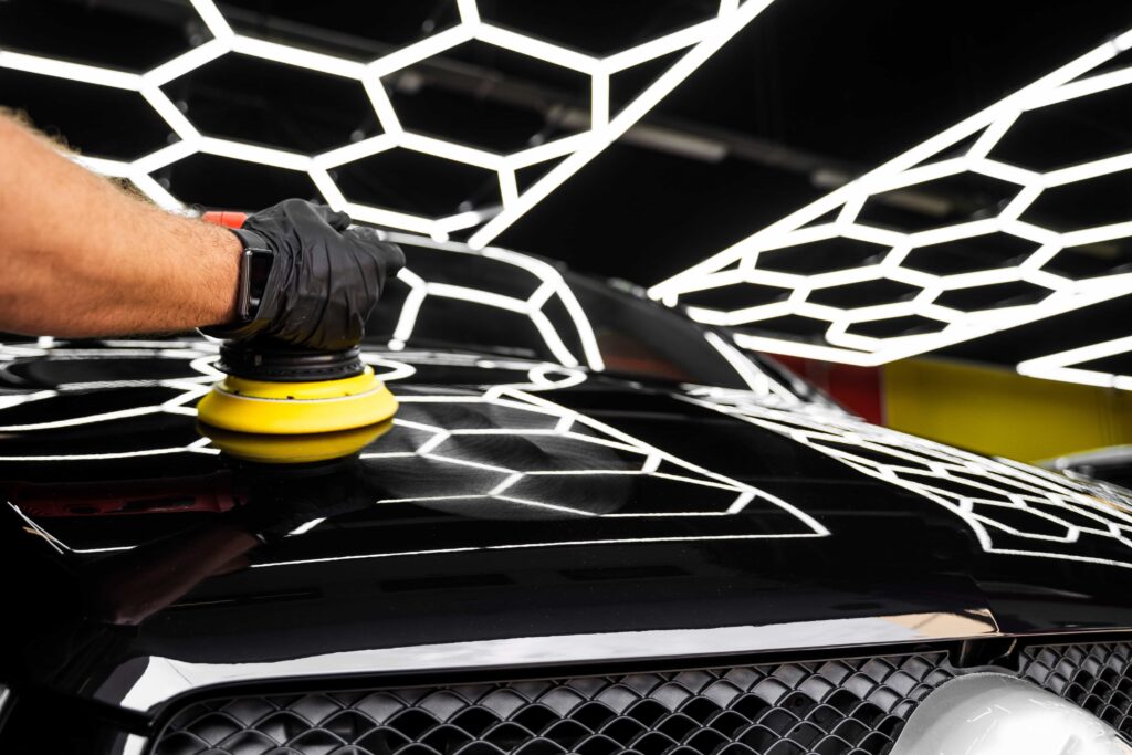 Professional technician performing precision paint correction with a rotary polisher on a black vehicle in a high-end detailing studio in Florida.