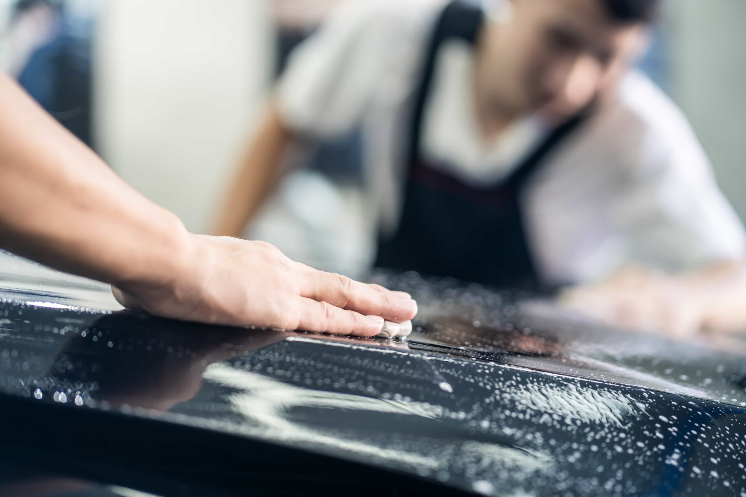 A professional detailer performing a clay bar treatment to remove surface contaminants from a black vehicle's paint during an auto detailing service and ceramic coating in Ocala, Florida.