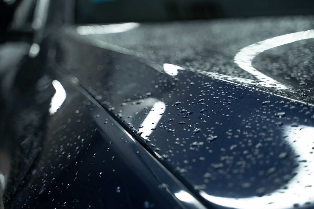 A close-up shot of tight water beads on a glossy, dark-colored car hood reflecting studio lights after a professional ceramic coating service in Phoenix, Arizona.
