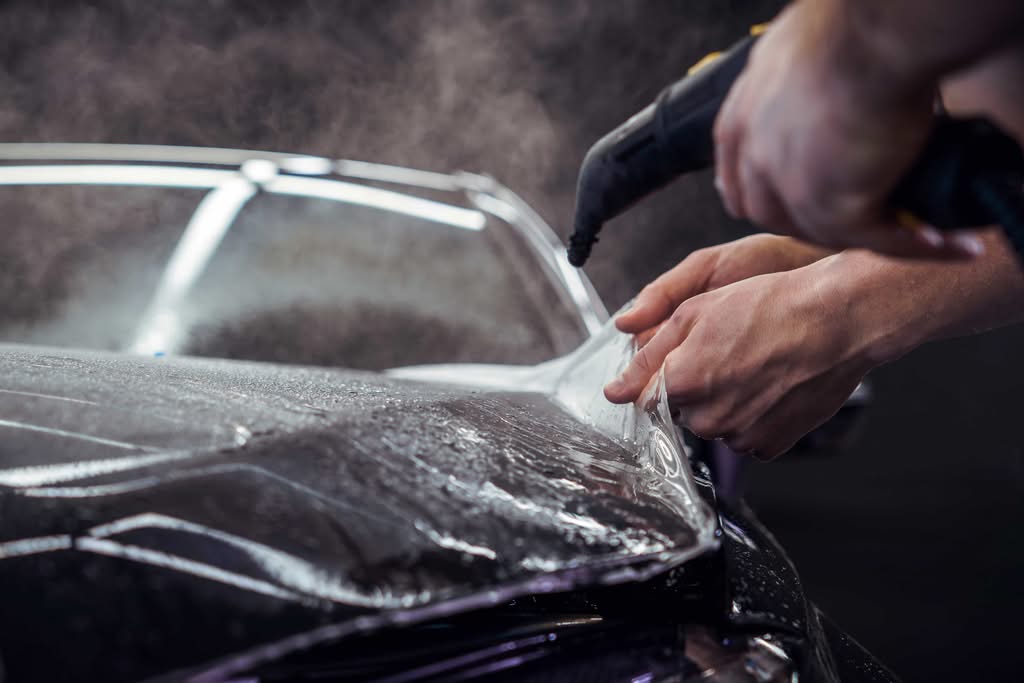 A detailed close-up of a high-end clear paint protection film or ceramic barrier layer being applied wet to a black vehicle's hood during a comparative ceramic coating vs traditional wax service in Ocala, Florida.
